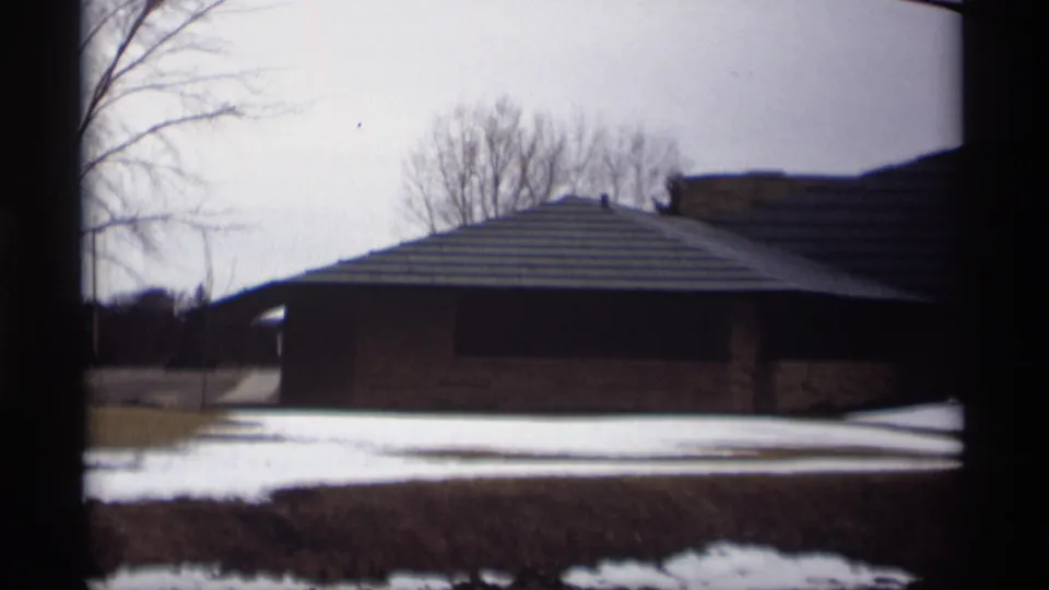 1966 Madison, Wisconsin 8mm frame showing a snow-dusted exterior with bare trees and a low brick building beyond dark foreground framing.