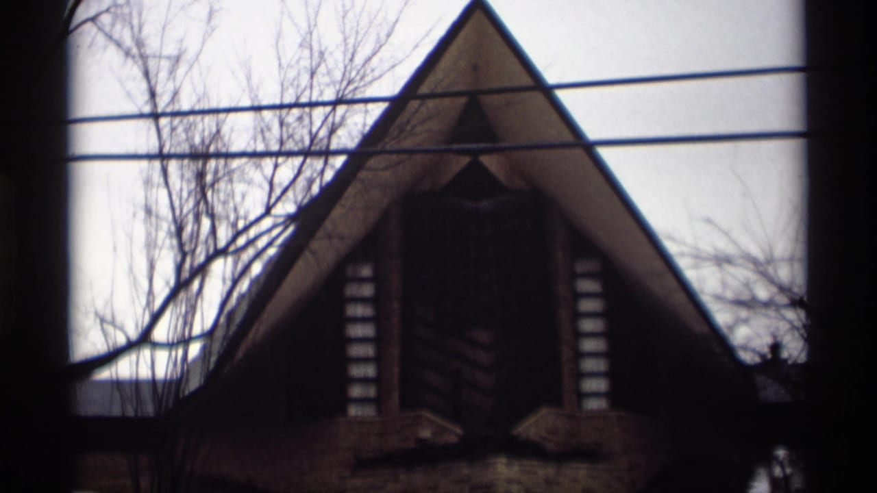 1966 Madison, Wisconsin 8mm frame of a steep triangular roofline, dark central opening, overhead wires, and leafless winter branches.