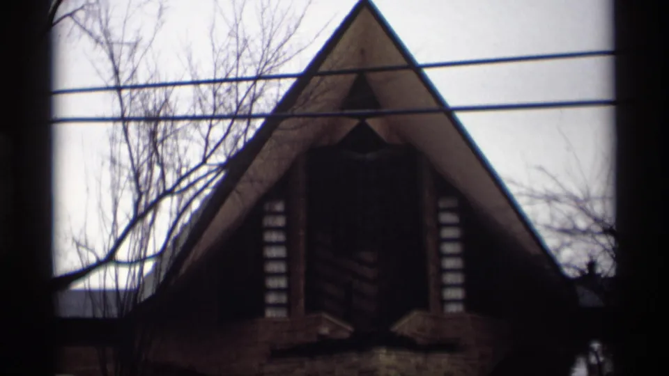 1966 Madison, Wisconsin 8mm frame of a steep triangular roofline, dark central opening, overhead wires, and leafless winter branches.