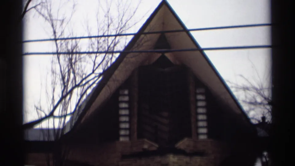 Closer 1966 Madison 8mm view of the pitched-roof facade, overhead wires, leafless branches, and dark foreground border.
