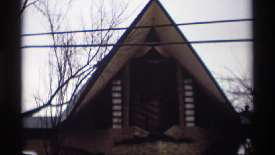 1966 Madison, Wisconsin frame showing the pitched-roof building front, bare branches, utility wires, and muted winter light.