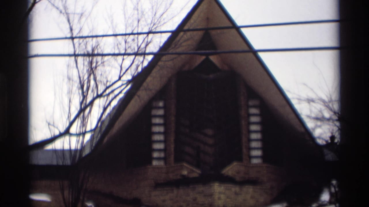 1966 Madison, Wisconsin 8mm frame of a modernist A-frame building in winter, partly obscured by window framing, bare trees, and overhead lines.