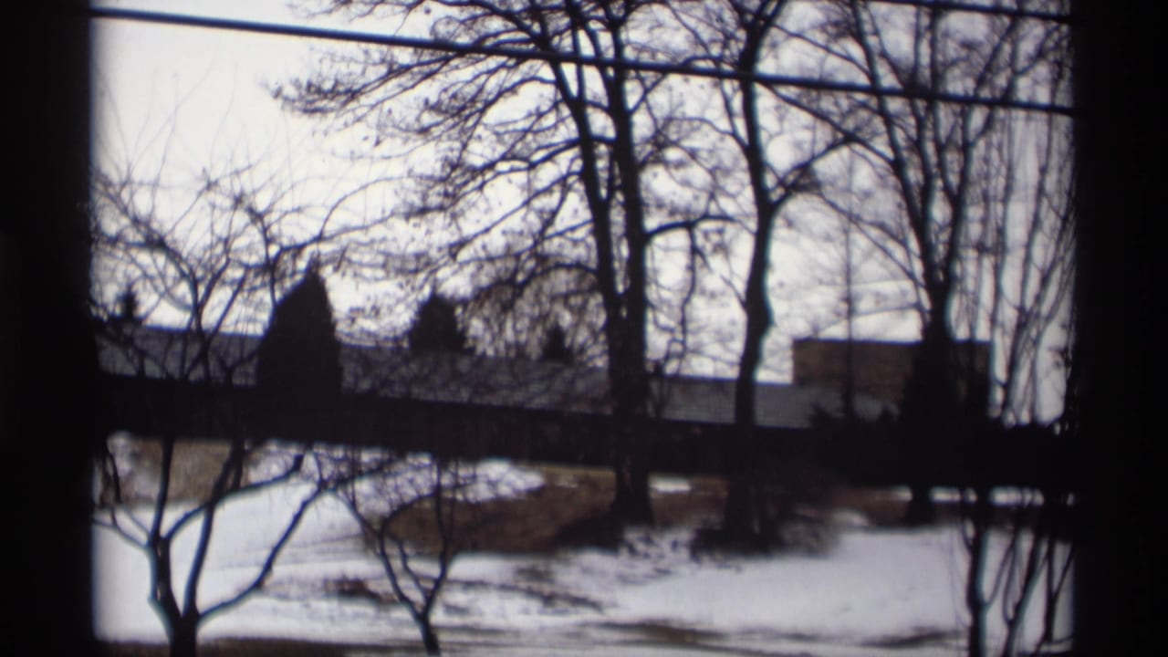 1966 Madison, Wisconsin winter view across snow and bare trees toward a distant modernist structure, seen through a dark window edge.