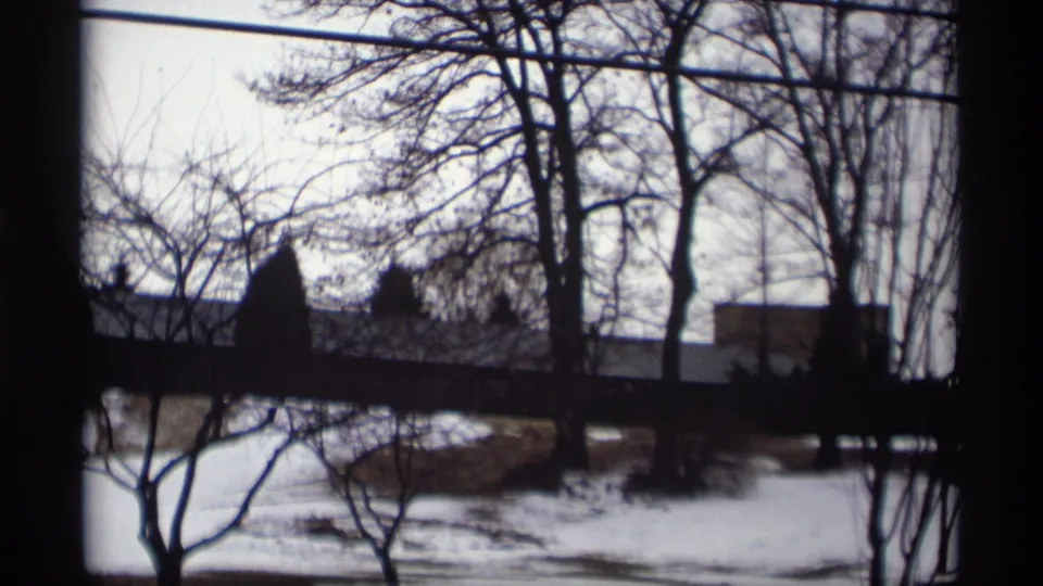 1966 Madison, Wisconsin home-movie frame looking across a snowy field and winter trees toward a partially obscured modernist building.
