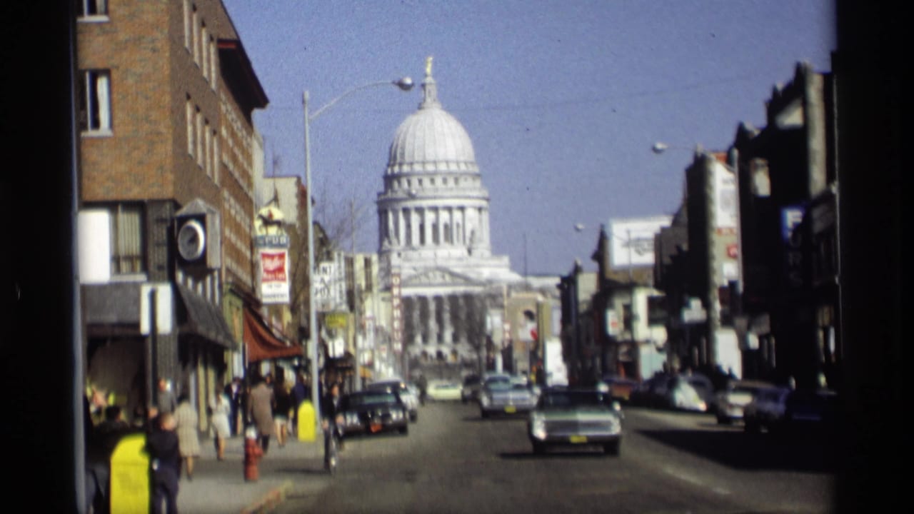 Similar street view toward the capitol with traffic, storefronts, sidewalks, and pedestrians.