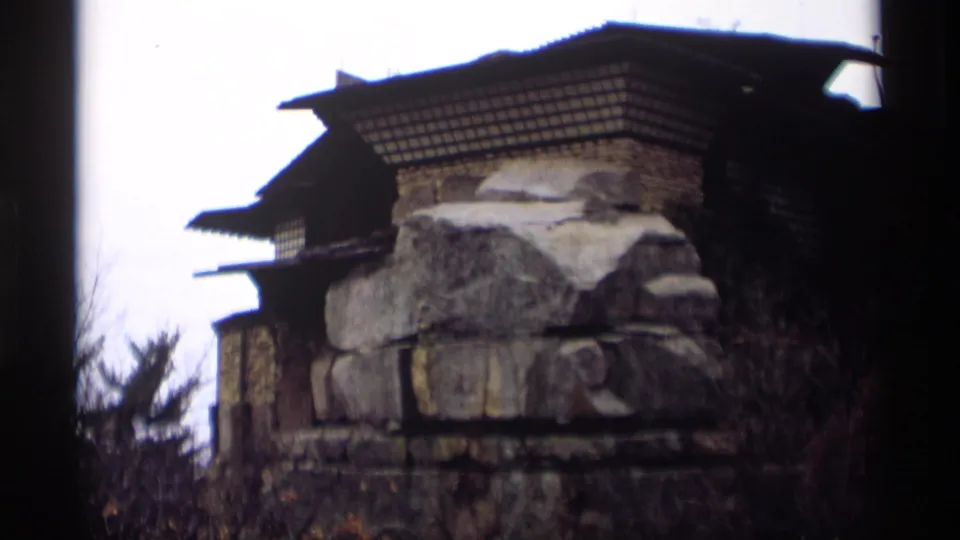 Rustic stone-and-wood building detail with heavy masonry, dark roof edges, and surrounding branches.