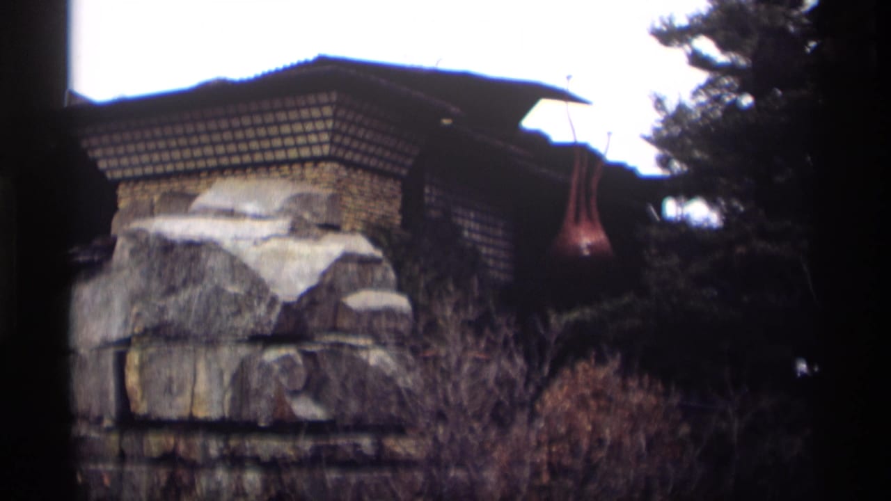 Stone structure and roofline partly framed by trees and dark film edges.