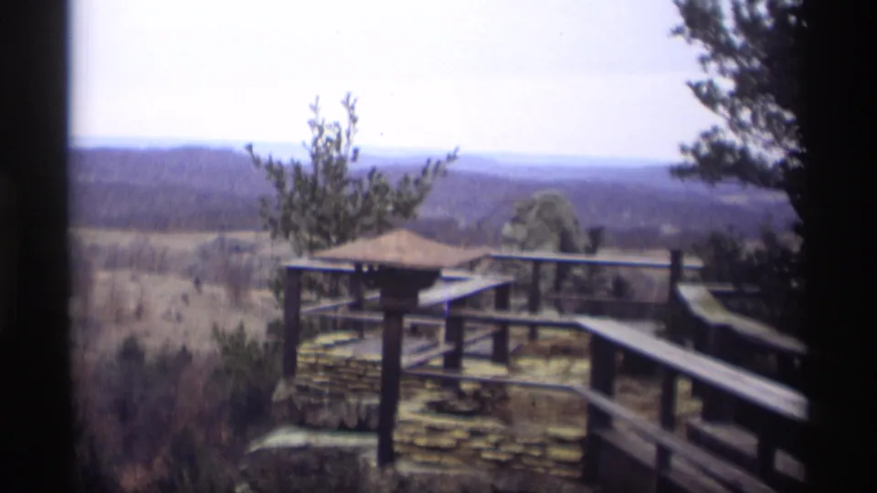 1966 Madison-area 8mm frame looking from a wooden deck toward fields, trees, and distant rolling hills under a pale sky.