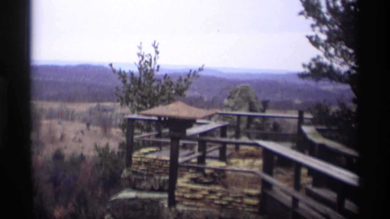 Wooden overlook railing and stone ledge facing a distant tree-covered landscape.
