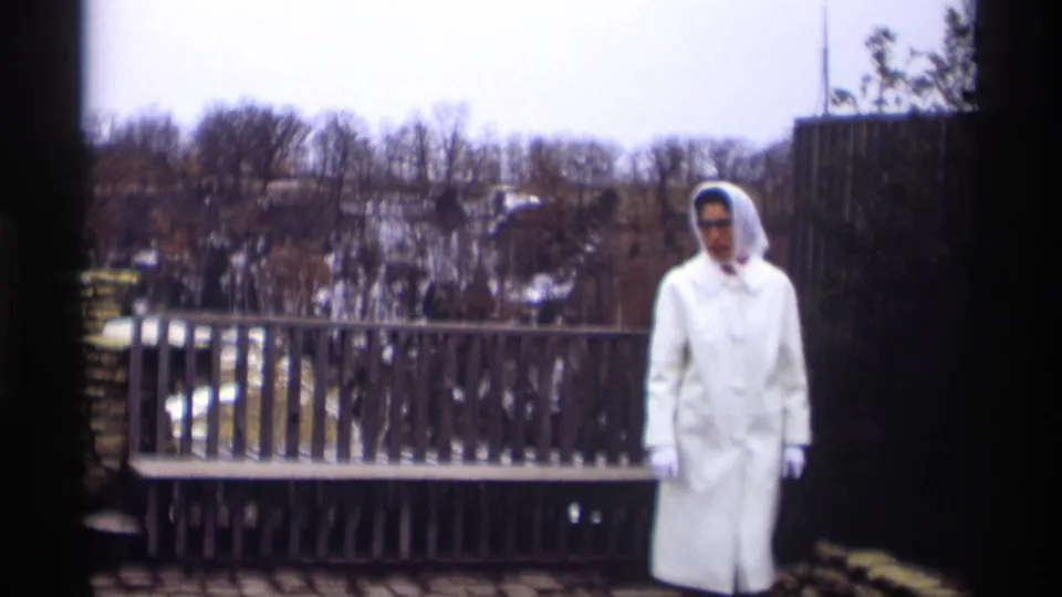A woman in a white coat and head covering appears beside a wooden railing at the Madison overlook in 1966 home-movie footage.