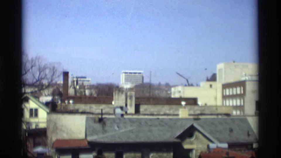 1966 Madison skyline view with residential rooftops, chimneys, low mid-century buildings, and a distant high-rise.