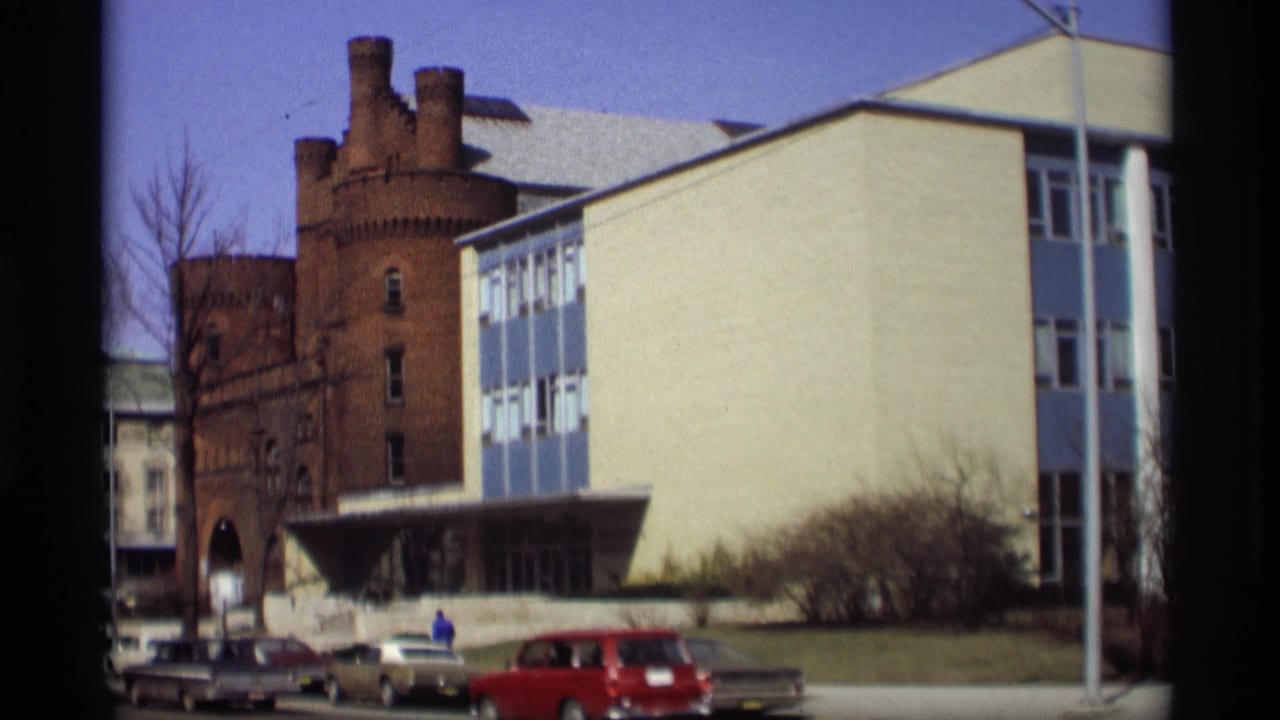 Blue-and-white building beside a brick tower with parked cars on a sunny street.