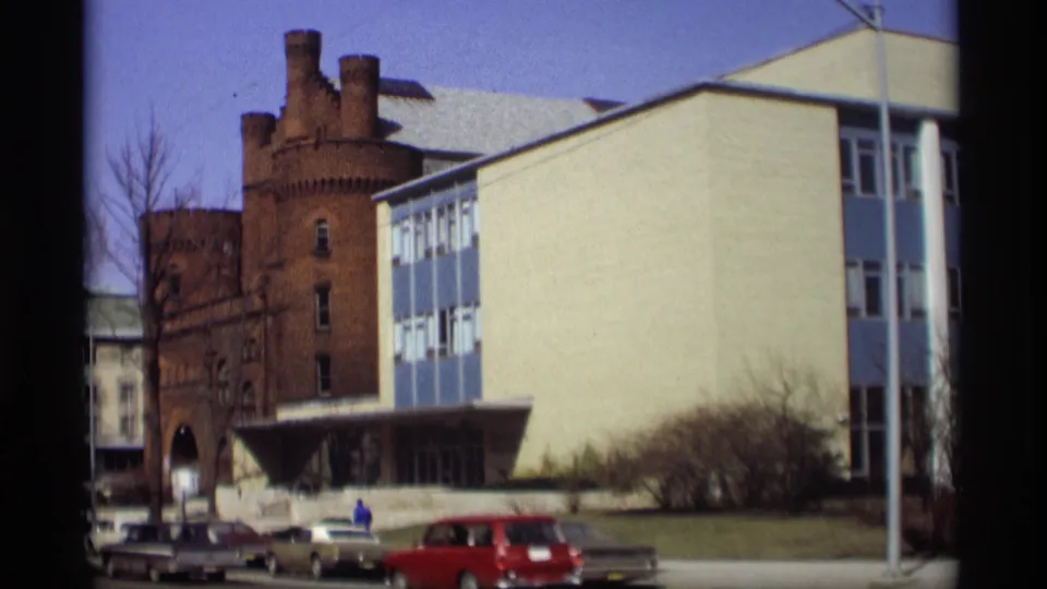 1966 Madison street view showing a modern blue-and-white building beside an older brick tower, with parked cars in front.