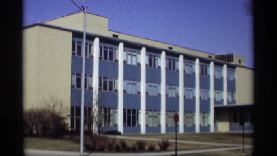 1966 Madison view of a modern blue-and-white building with tall white columns, shrubs, a streetlight, and a stop sign.