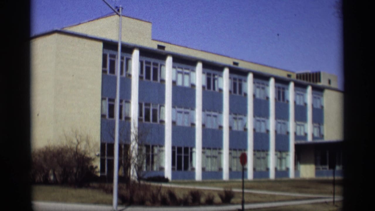 Blue-and-white modern building with white columns beside a lawn and stop sign.