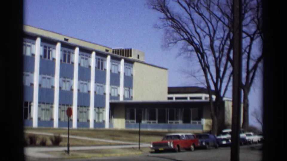 1966 Madison frame showing the modern facade with white columns, a stop sign, bare trees, and a red station wagon.