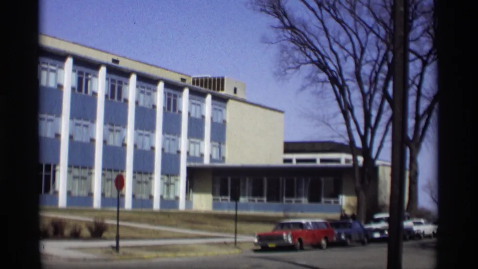 Final 1966 Madison view of the modern blue-and-white building framed by bare trees and parked cars.