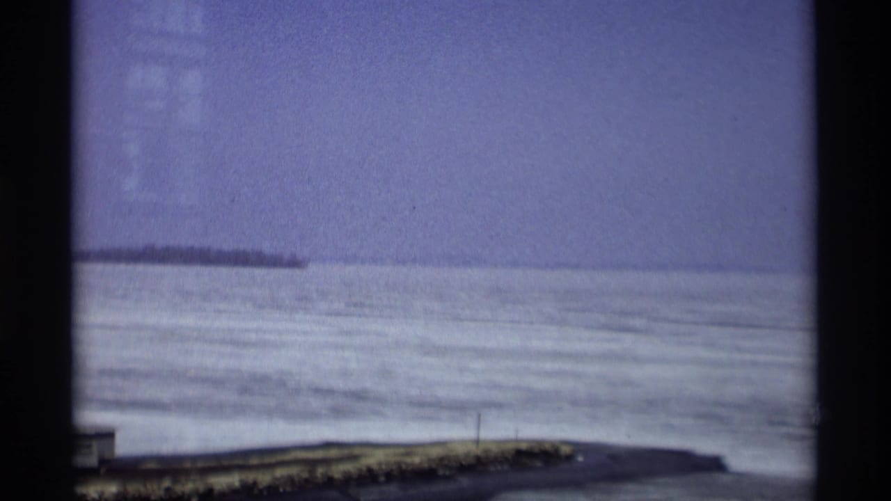 1966 Madison, Wisconsin home-movie view of a frozen lake with distant shoreline under a pale sky.
