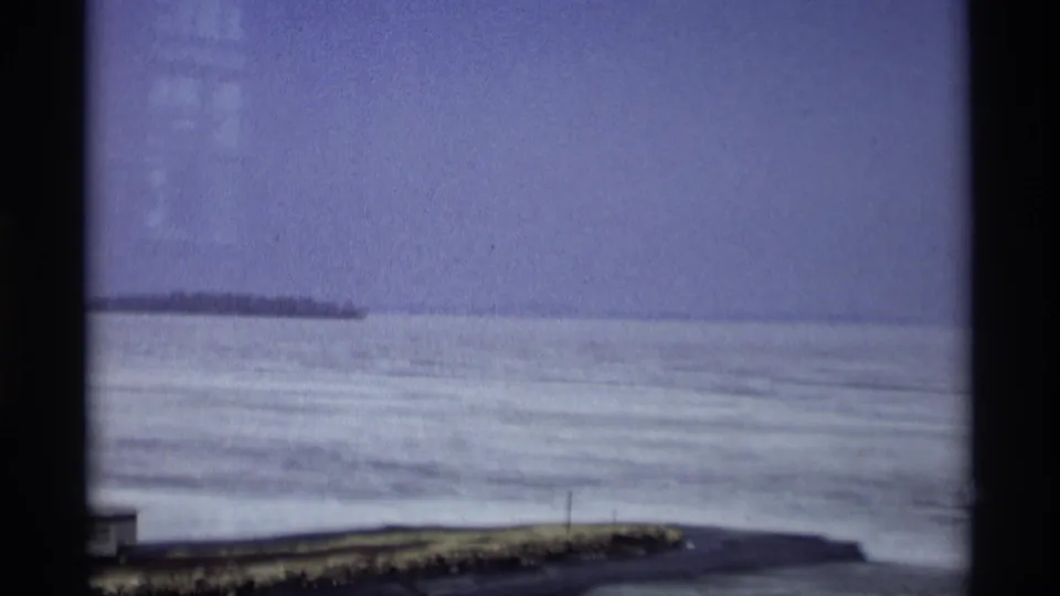 1966 Madison, Wisconsin home-movie view of a frozen lake with distant shoreline under a pale sky.