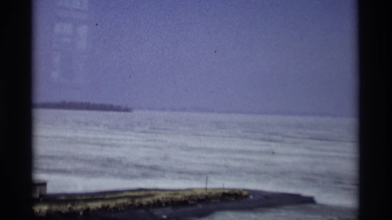 Madison lake ice and distant shore appear in a grainy 1960s 8mm frame with dark gate edges.