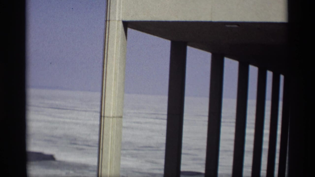 Concrete columns and roof overhang frame a pale body of water.