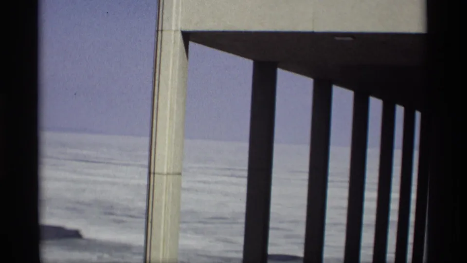 1966 Madison-area 8mm frame showing modernist concrete pillars looking out toward calm water and a distant shoreline.
