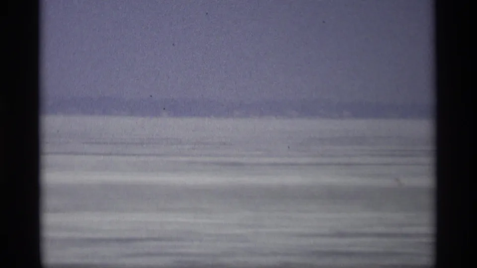1966 Madison, Wisconsin frame showing a quiet lake expanse with horizontal water texture, pale sky, and dark foreground framing.