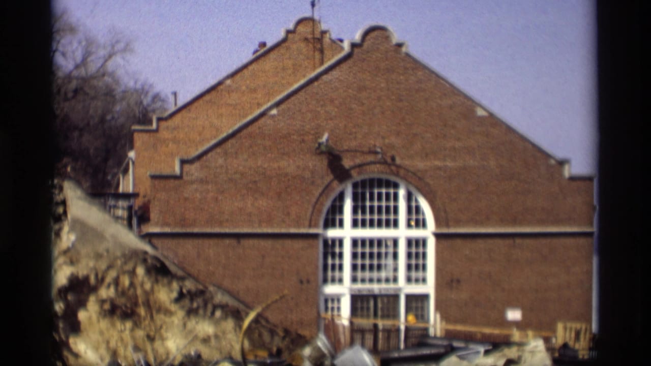 1966 Madison frame of a large brick building with a stepped gable and arched white-framed window beside a snowy winter bank.
