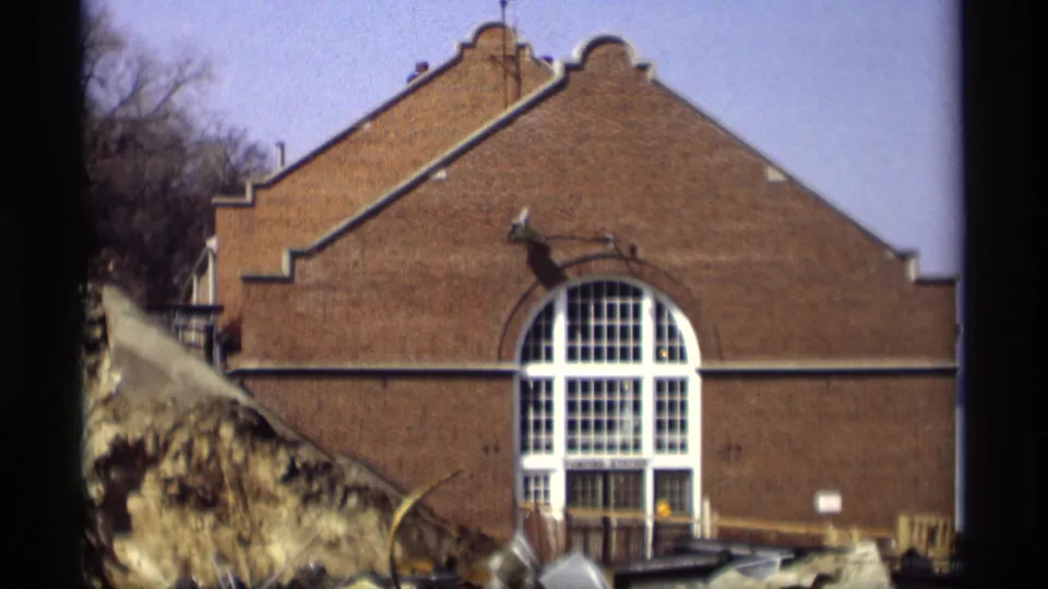1966 Madison frame holding on the brick gabled building, its arched window, and the rough snowy bank in front.