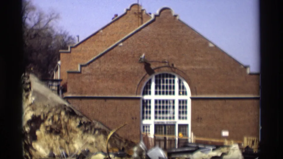 1966 Madison frame showing the same brick building with stepped gable, arched window, winter trees, and snow-covered ground nearby.