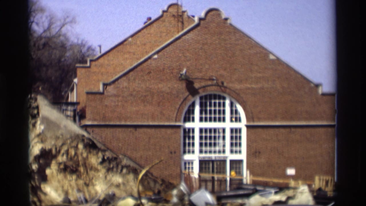 1966 Madison 8mm frame showing a brick pumping station facade with a tall arched window and rough foreground material.