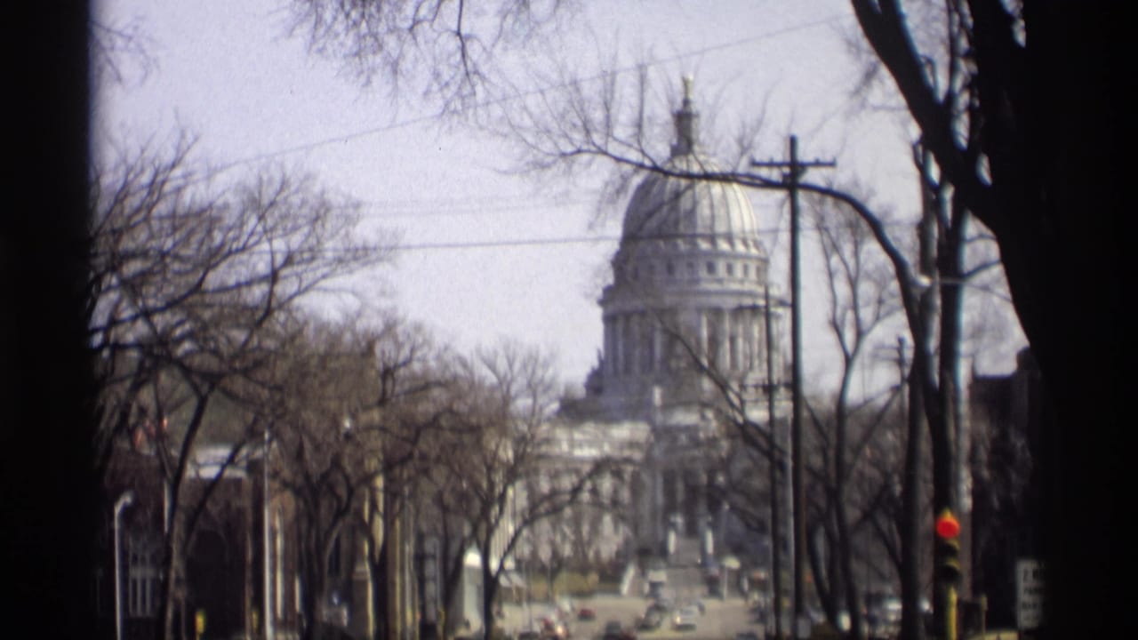 1966 8mm view of the Wisconsin State Capitol in Madison, partly framed by bare trees, wires, and a traffic signal.