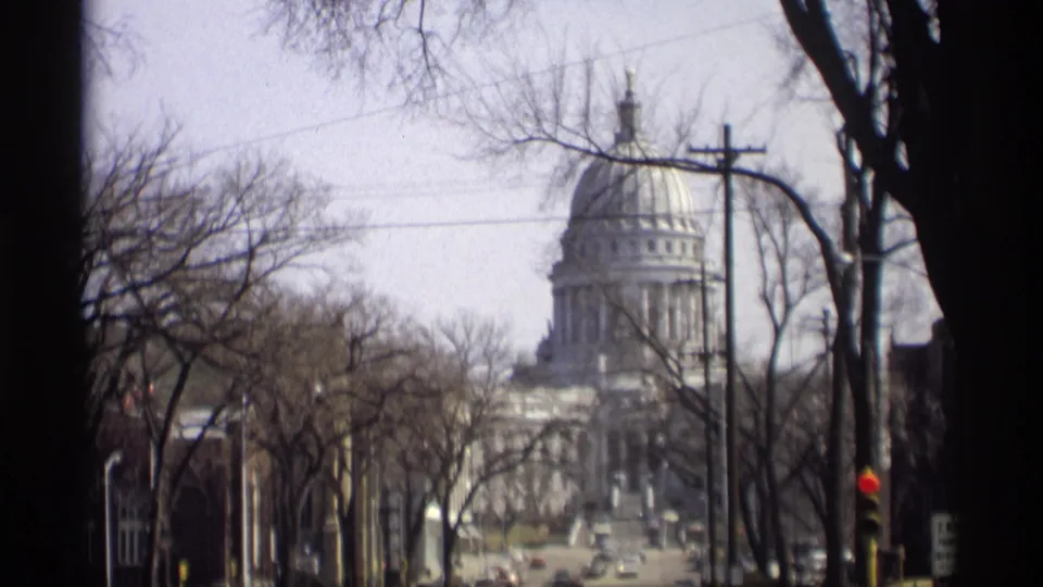 1966 8mm view of the Wisconsin State Capitol in Madison, partly framed by bare trees, wires, and a traffic signal.