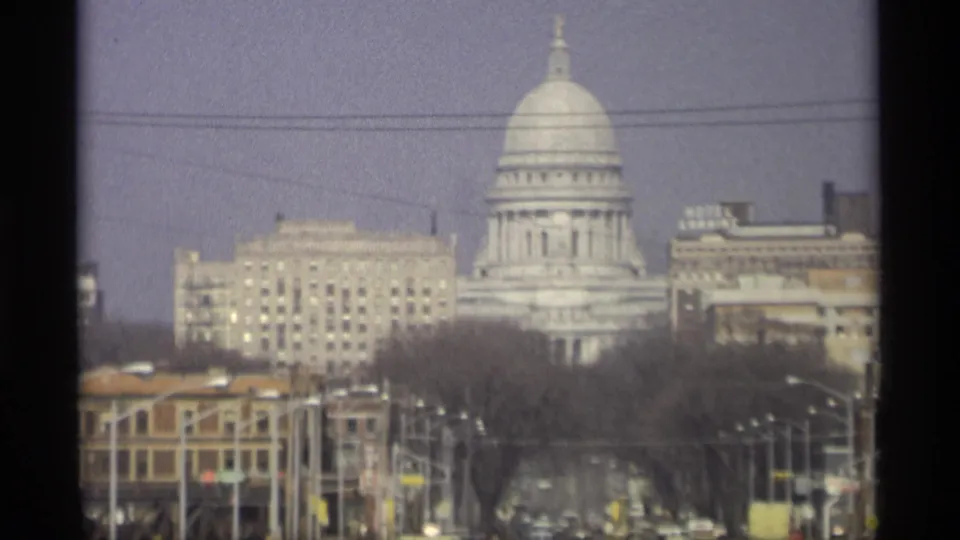 Distant 1966 view of the Wisconsin State Capitol dome above Madison buildings, with traffic and trees in the foreground.
