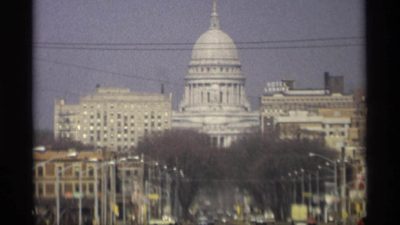 Capitol dome centered behind downtown buildings, trees, wires, and faint traffic.