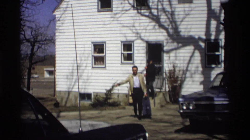 In the Madison driveway scene, the suited man moves forward with a suitcase while another adult follows from the house.