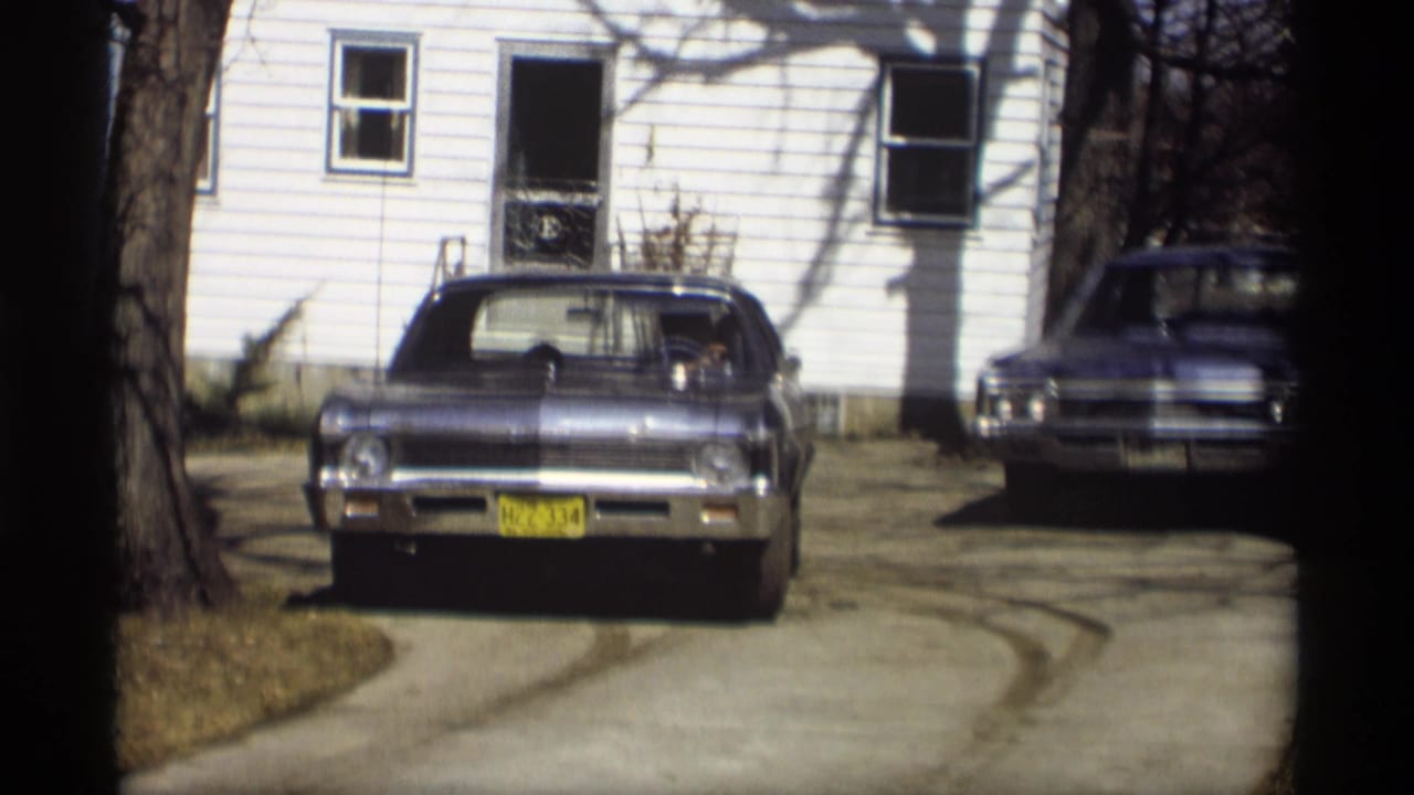 Blue Chevrolet Impala remains centered in a Madison driveway, with a second vintage car parked near the white house behind it.