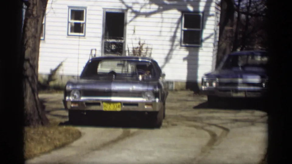Blue Chevrolet Impala remains centered in a Madison driveway, with a second vintage car parked near the white house behind it.
