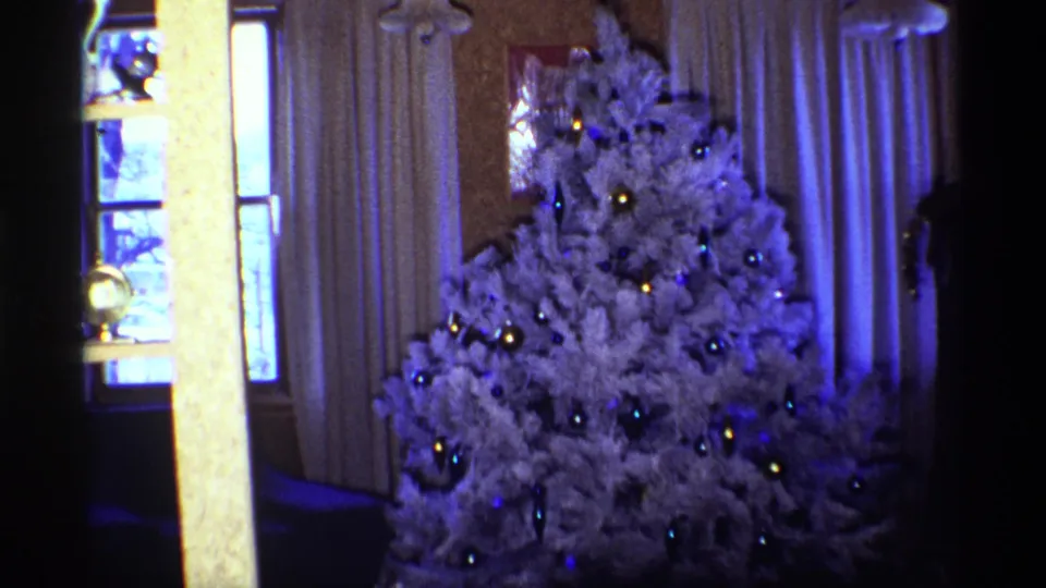 1968 Chicago 8mm still of a white artificial Christmas tree with metallic ornaments and small lights beside a window.