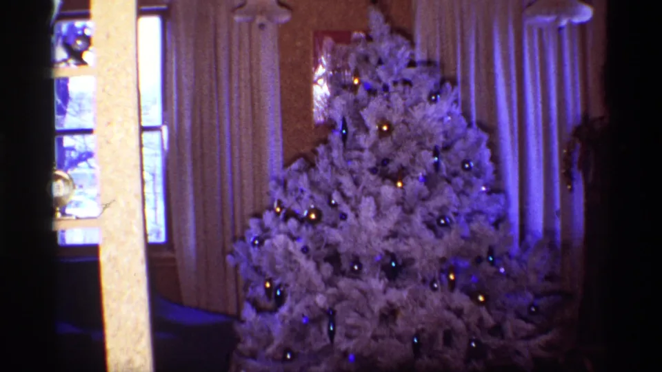 White artificial Christmas tree with shiny ornaments and warm room lighting in 1968 Chicago home-movie footage.