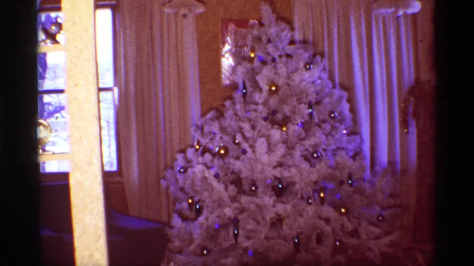 Close 8mm view of a white Christmas tree with blue and gold ornaments inside a Chicago home in 1968.