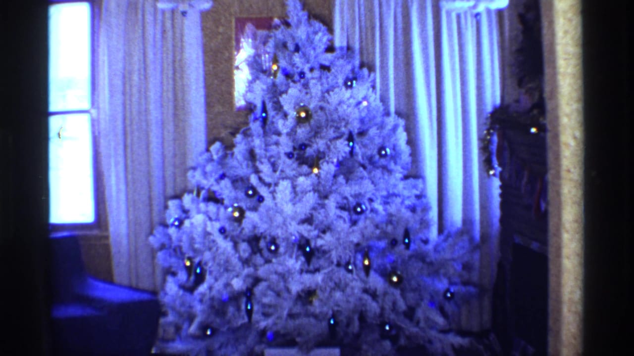 1968 Chicago 8mm frame showing a white Christmas tree with blue and gold ornaments beside curtains and a bright window.