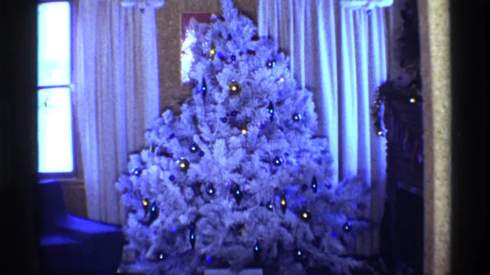 1968 Chicago 8mm frame showing a white Christmas tree with blue and gold ornaments beside curtains and a bright window.
