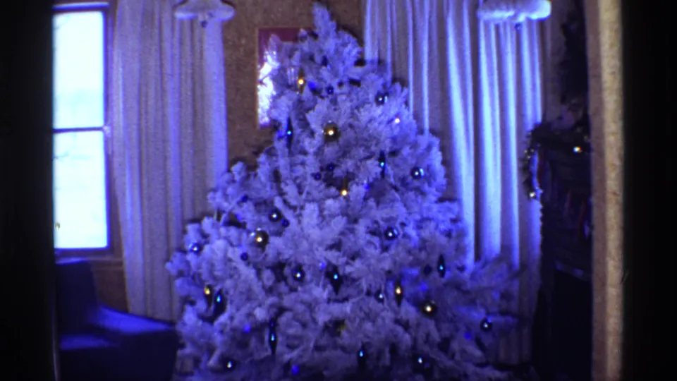 Blue-shifted 8mm frame from 1968 Chicago showing a white Christmas tree and living-room curtains in soft daylight.