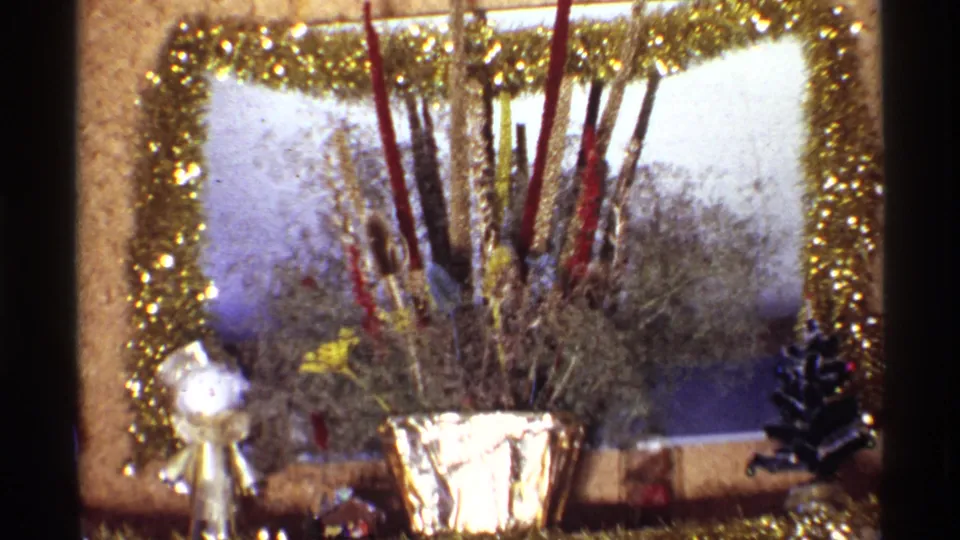 1968 Chicago home-movie close-up of a holiday centerpiece with metallic gold framing, dried floral stems, and a small silver figure.