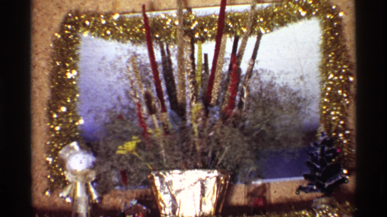 Christmas mantel detail with gold garland, foil vase, tall sticks, angel figure, and small tree.
