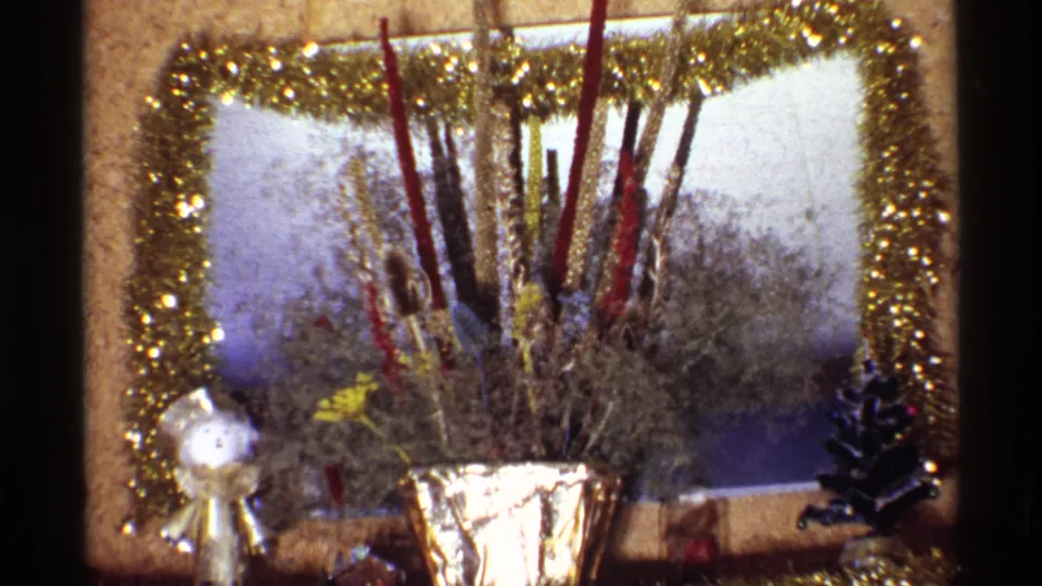 1968 Chicago home-movie frame with a closer view of the Christmas mantel, showing tinsel garland, a shiny vase, upright sticks, and small decorations.