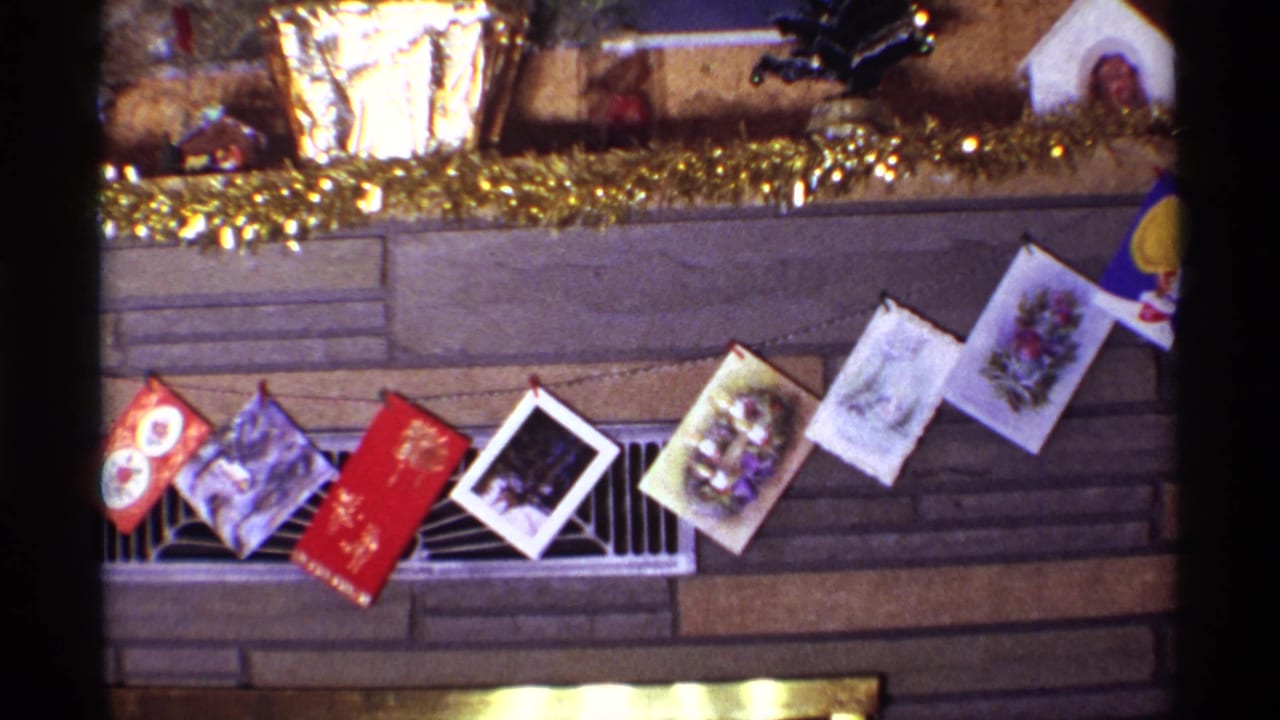 Decorated fireplace mantel with tinsel, holiday cards, foil planters, and a small tabletop tree.