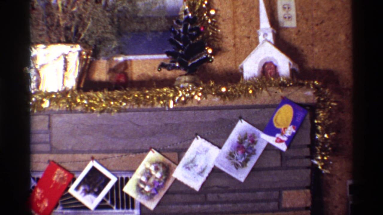 Tilted 1968 Chicago home-movie view of Christmas cards across a stone fireplace, with tinsel, planters, and small mantel decorations visible.