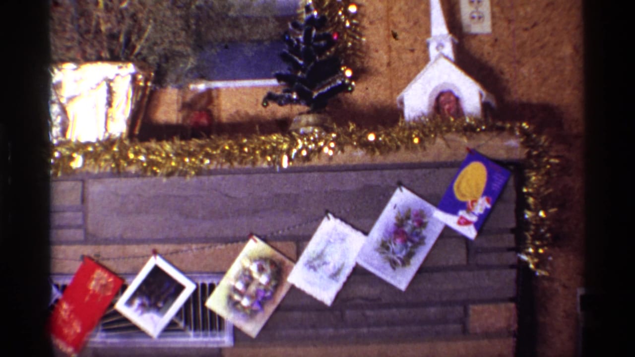 Christmas-decorated fireplace mantel with cards, tinsel, small tree, and church figurine.